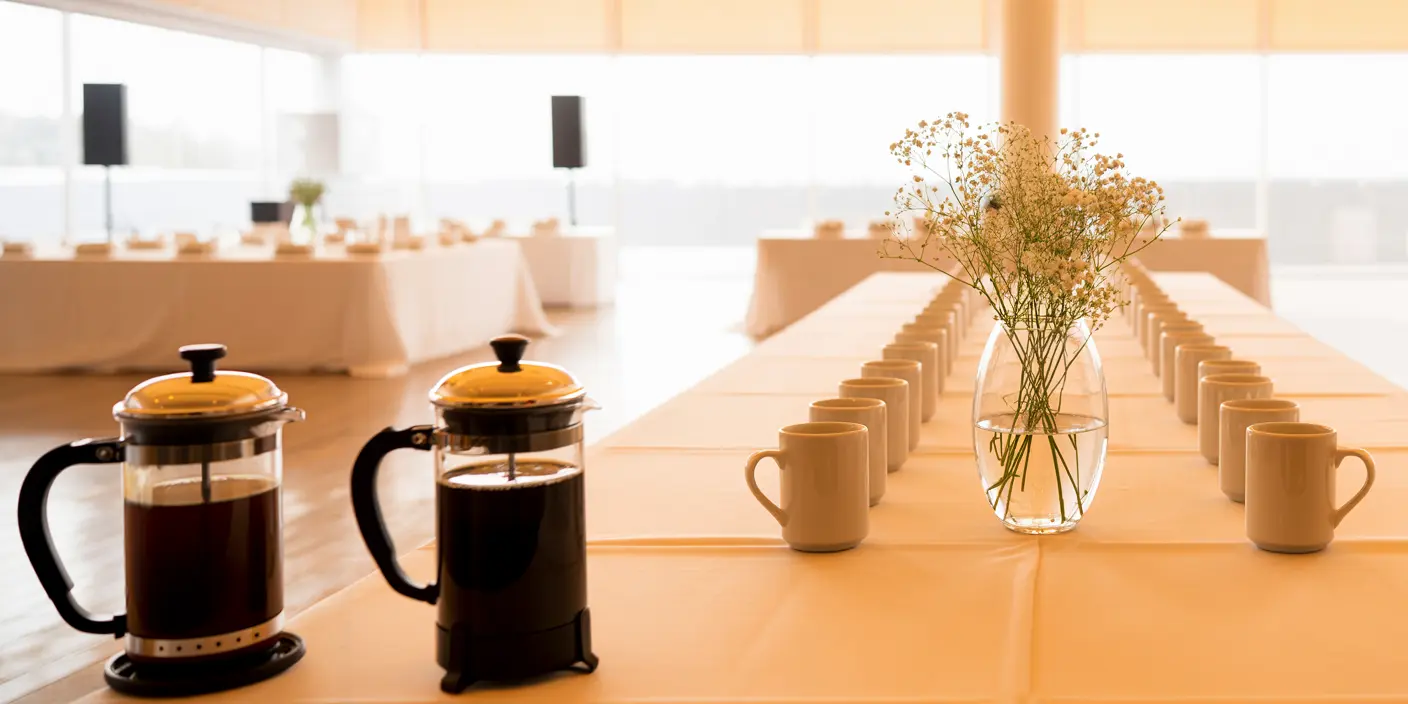 Prensas francesas y tazas blancas dispuestas sobre una mesa larga para una pausa de café