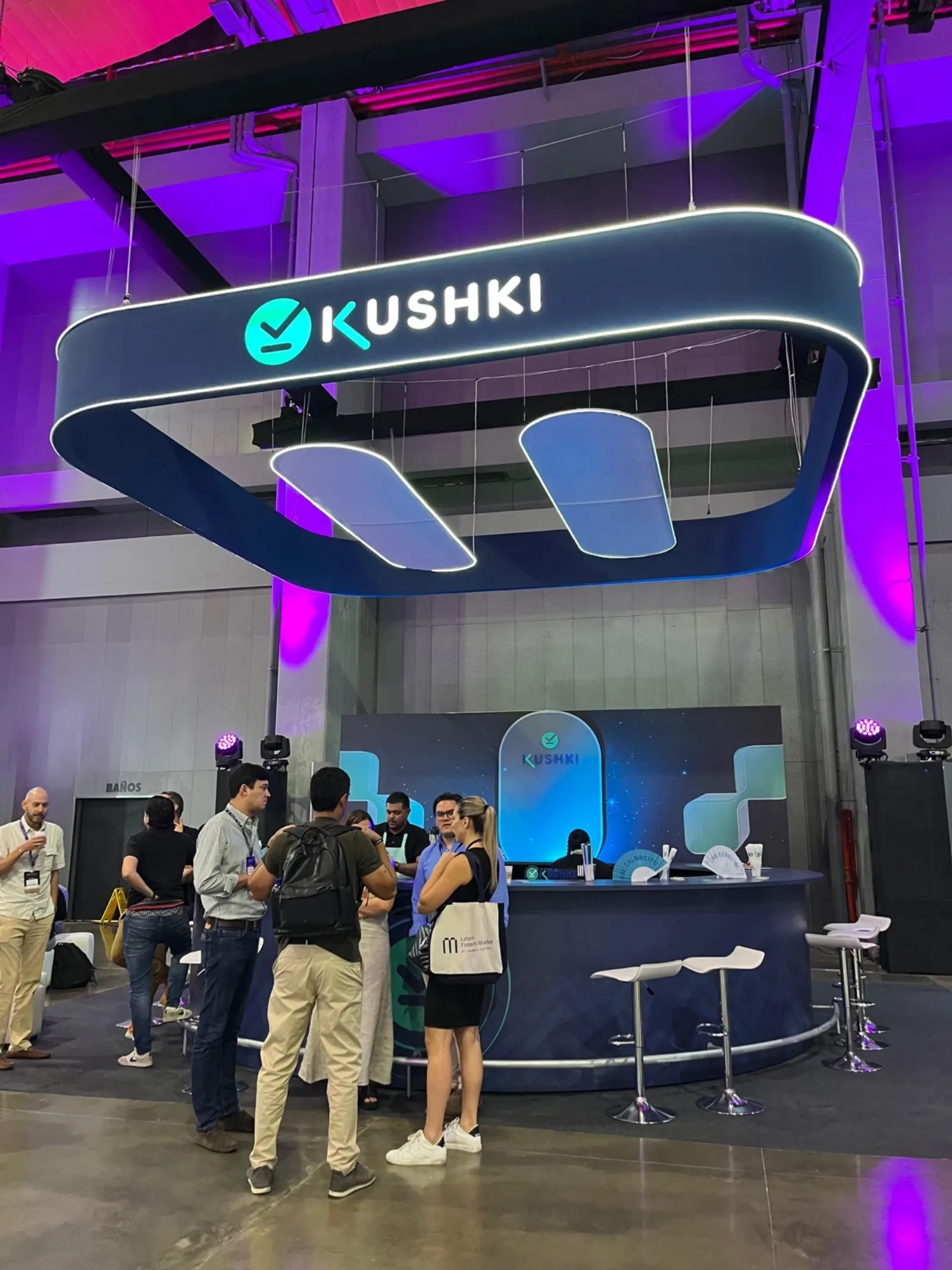 Visitantes conversando frente a la barra de bebidas del stand de KUSHKI en una feria en Barranquilla