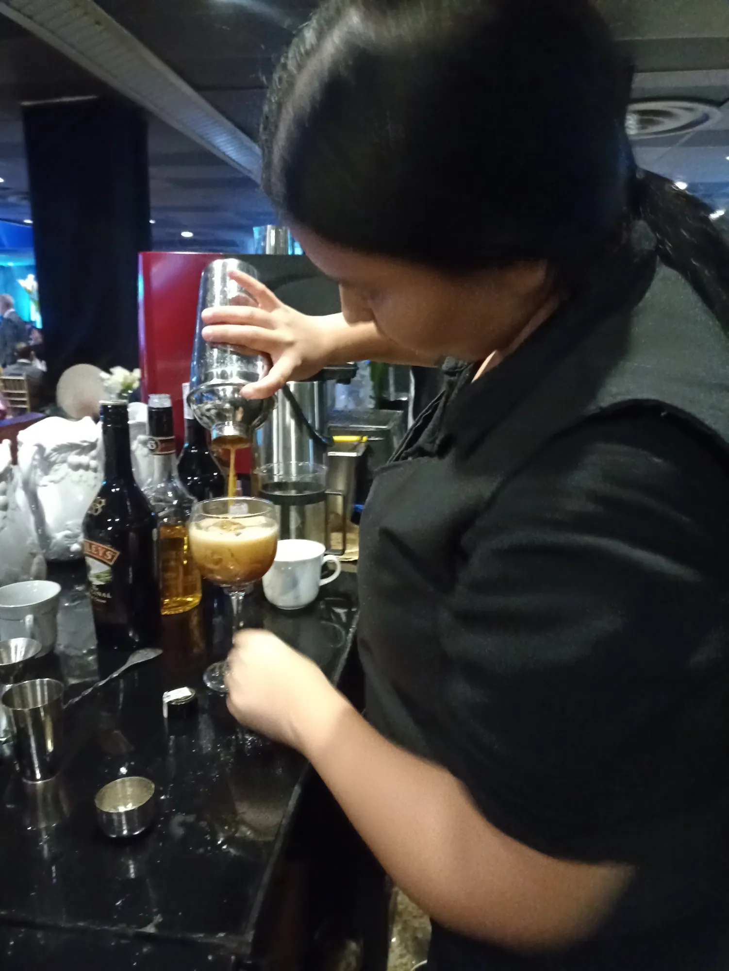 Bartender de Experiencia VINTO sirviendo un cóctel de café desde la coctelera a una copa, junto a botellas de crema irlandesa y licor en la barra