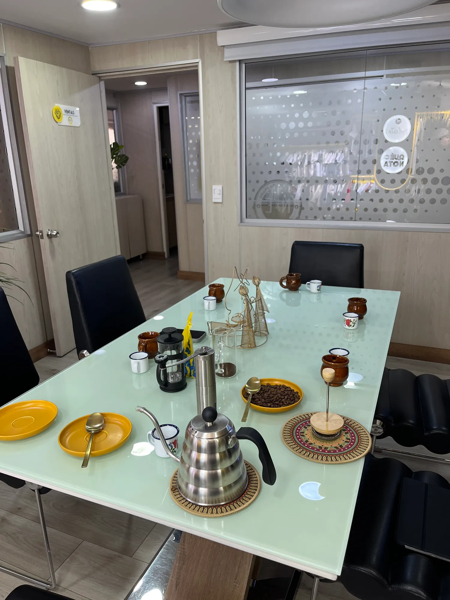 Coffee tasting table in a meeting room with a gooseneck kettle, a French press, a plate of roasted coffee beans and clay cups