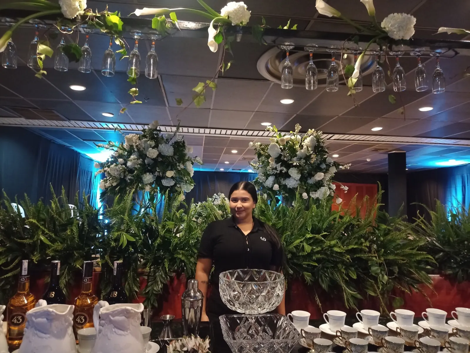 Integrante del equipo de servicio junto a una barra de café con tazas de porcelana y arreglos florales en un salón de eventos
