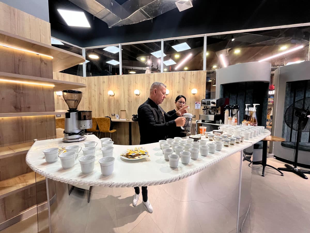 Barista de Experiencia VINTO preparando café en una barra blanca con tazas de porcelana y molino de café