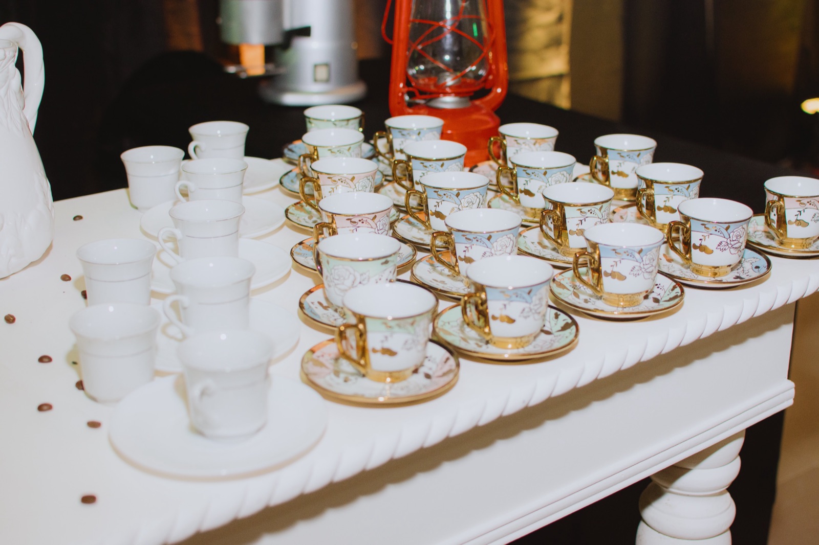Mesa blanca con tazas de porcelana con borde dorado listas para el servicio de café en una celebración