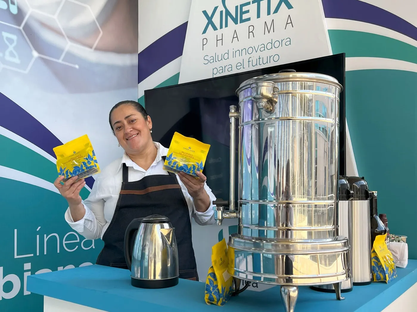 Barista de Experiencia VINTO muestra dos bolsas de Amar Café junto a un termo de acero en el espacio de Xinetix Pharma durante un congreso en Bucaramanga