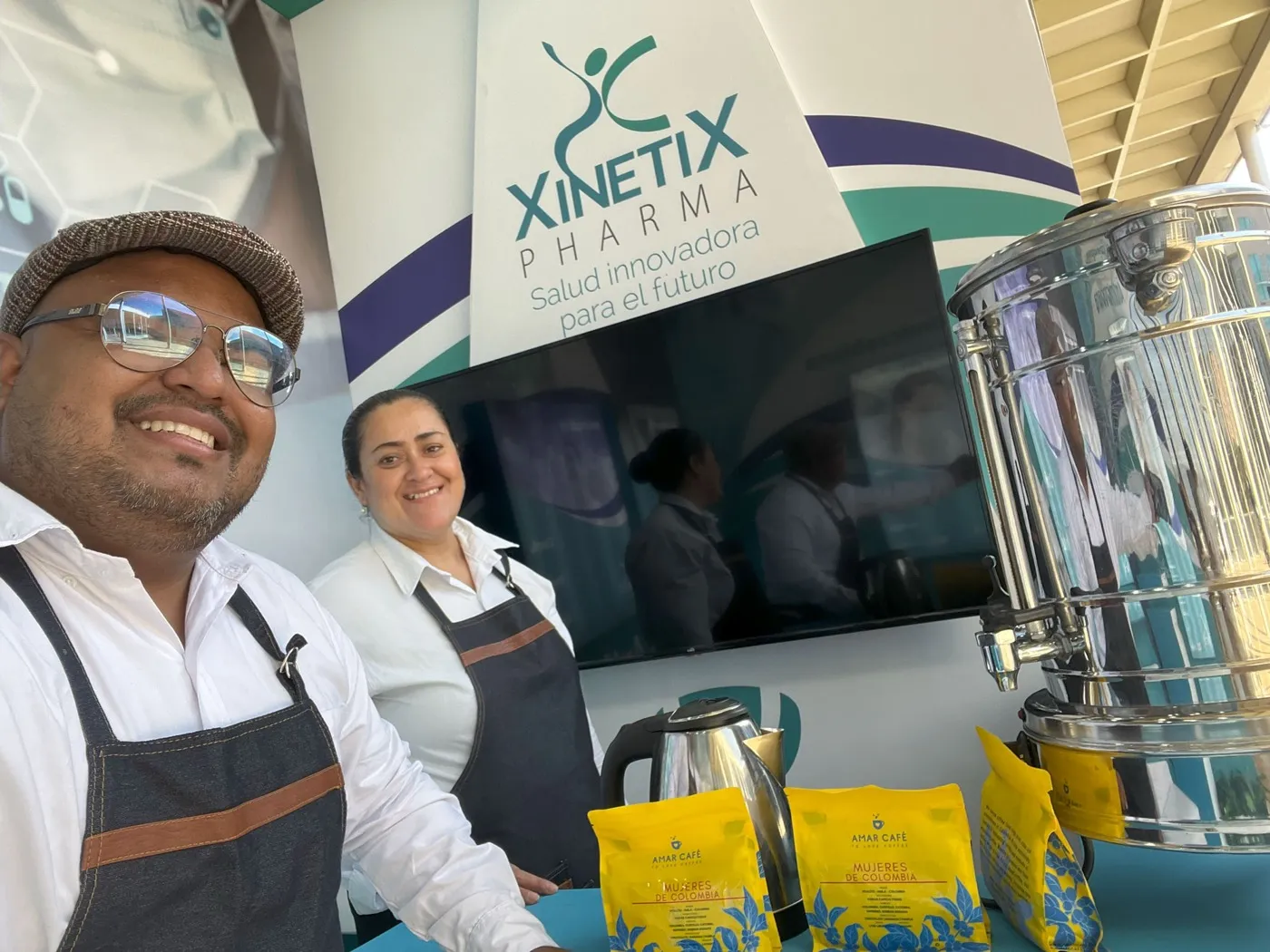 Dos baristas de Experiencia VINTO con delantal junto a un termo de café, un hervidor y bolsas de Amar Café en el espacio de Xinetix Pharma en Bucaramanga