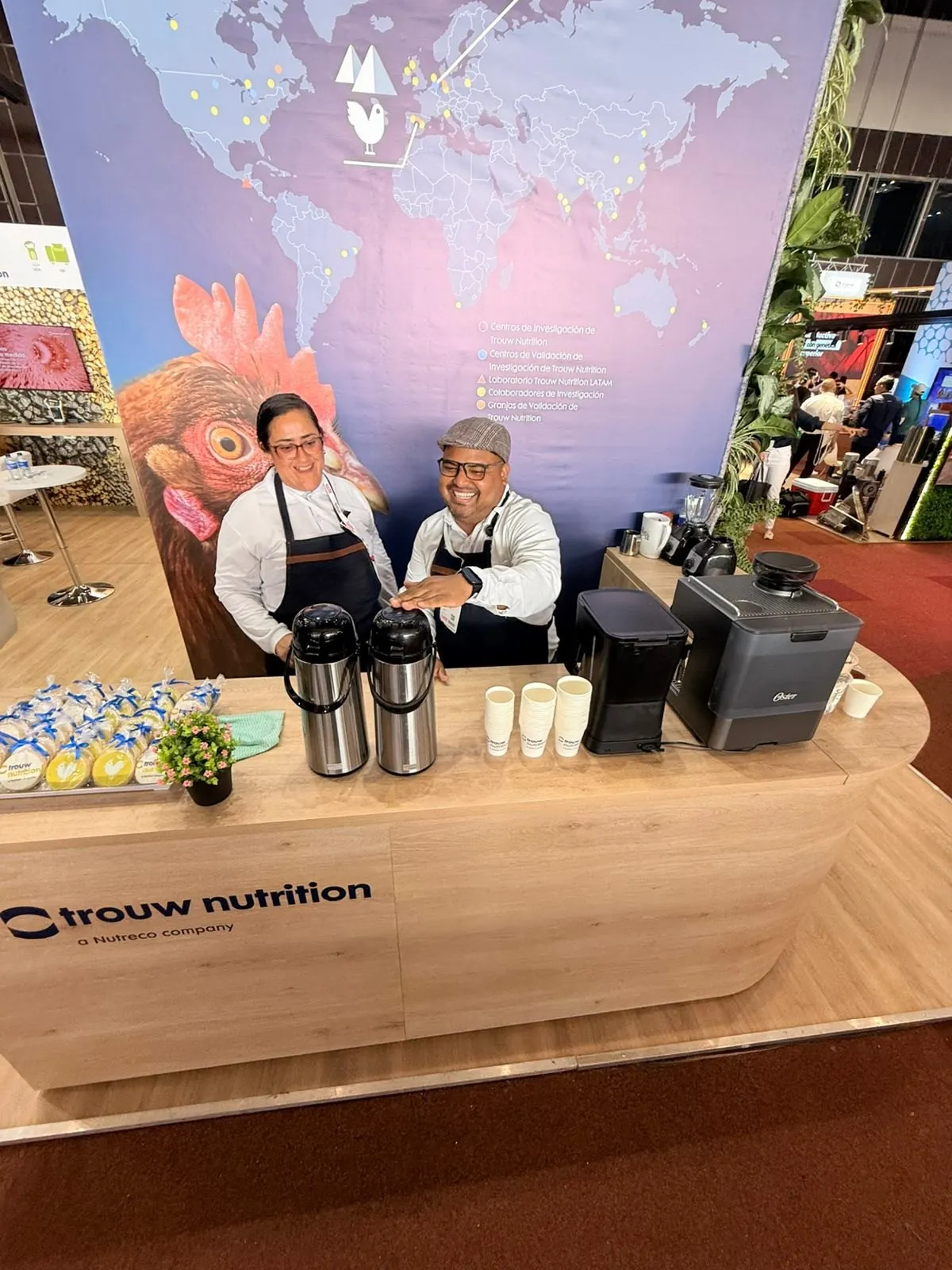 Dos baristas de Experiencia VINTO detrás de la barra de café con termos, vasos y galletas con la marca de Trouw Nutrition en Cali