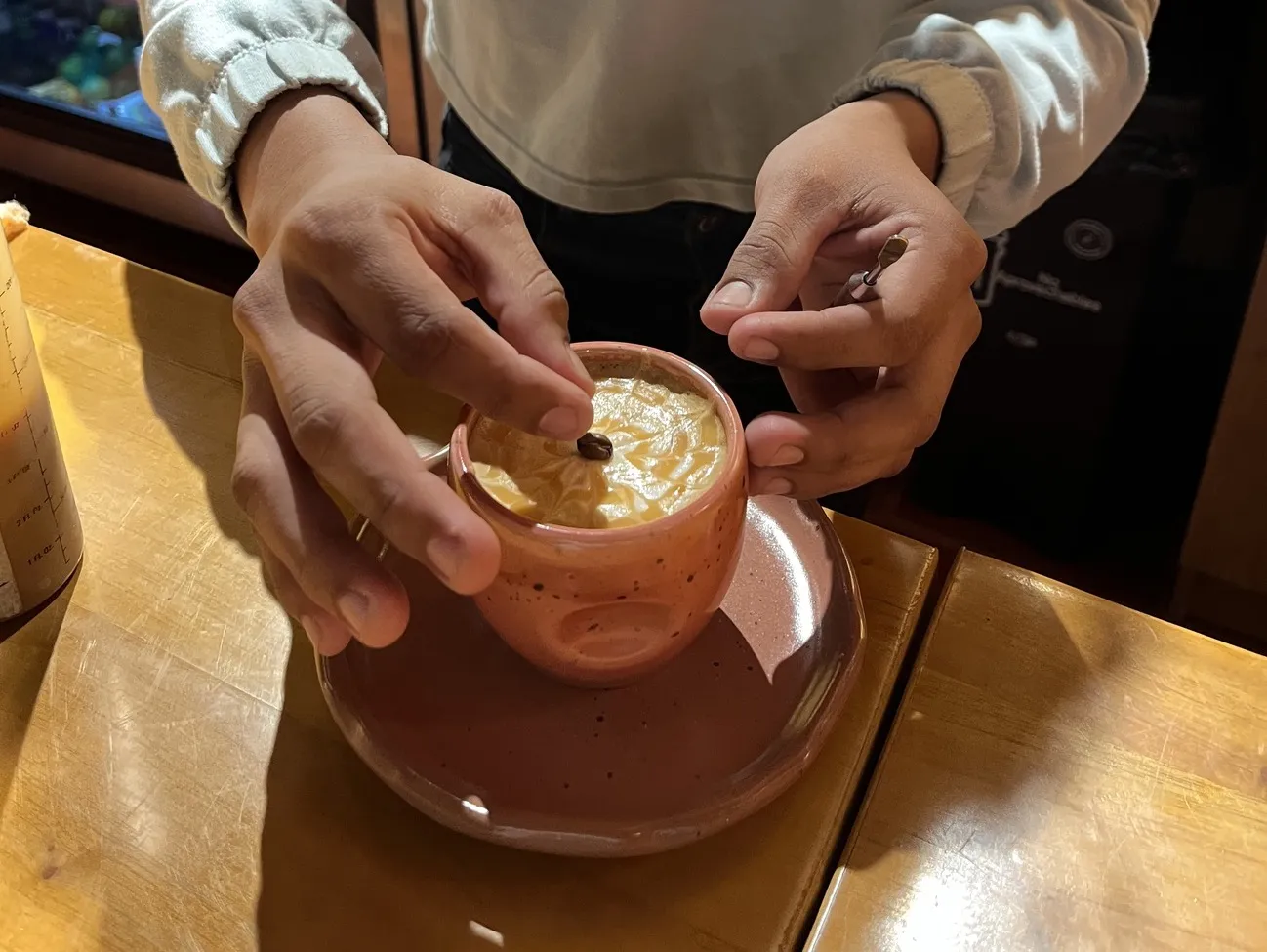 Manos de un barista poniendo un grano de café sobre la espuma de una bebida de café servida en una taza de cerámica