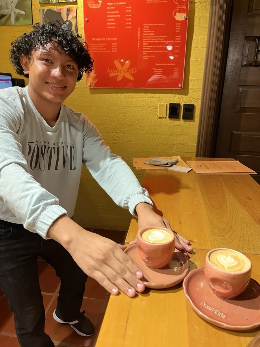 Barista junto a dos capuchinos con arte latte en tazas de cerámica sobre una barra de madera
