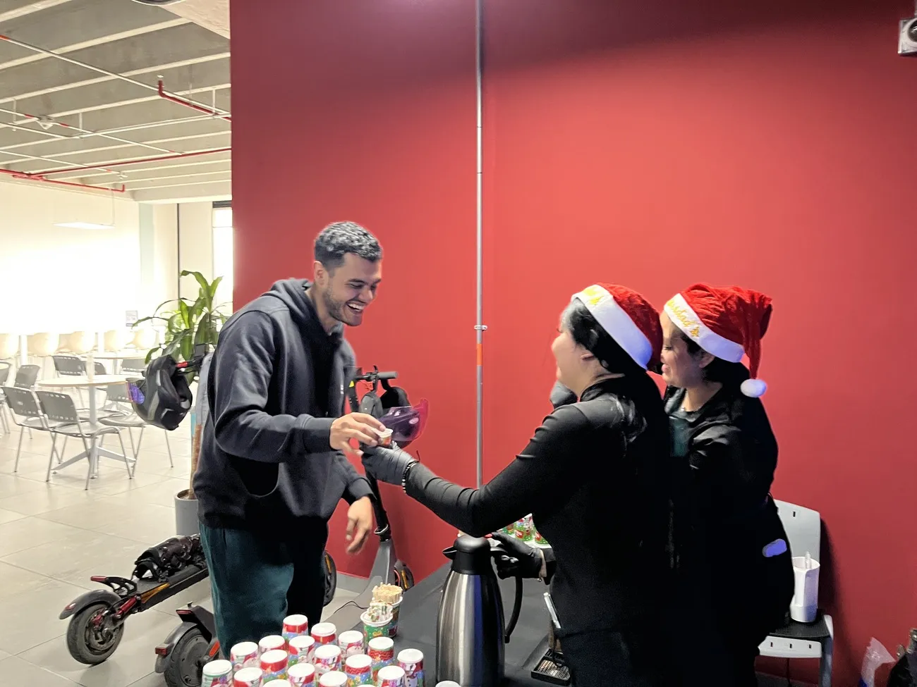 Baristas con gorros de Navidad sirviendo bebidas a un empleado en una estación de café dentro de una oficina