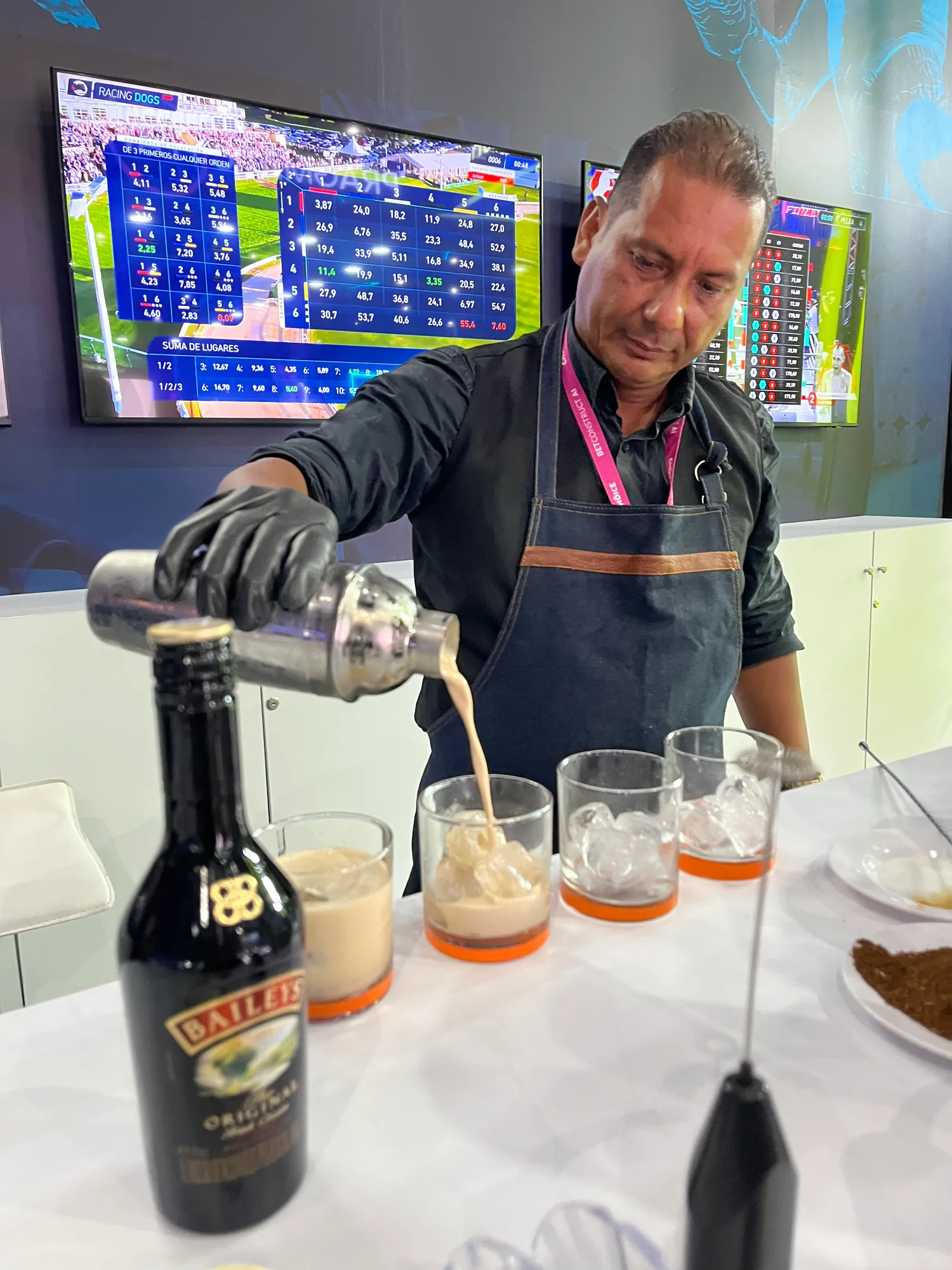 Bartender con guantes sirviendo un cóctel de café con crema de whisky irlandesa en vasos con hielo dentro de un stand de feria