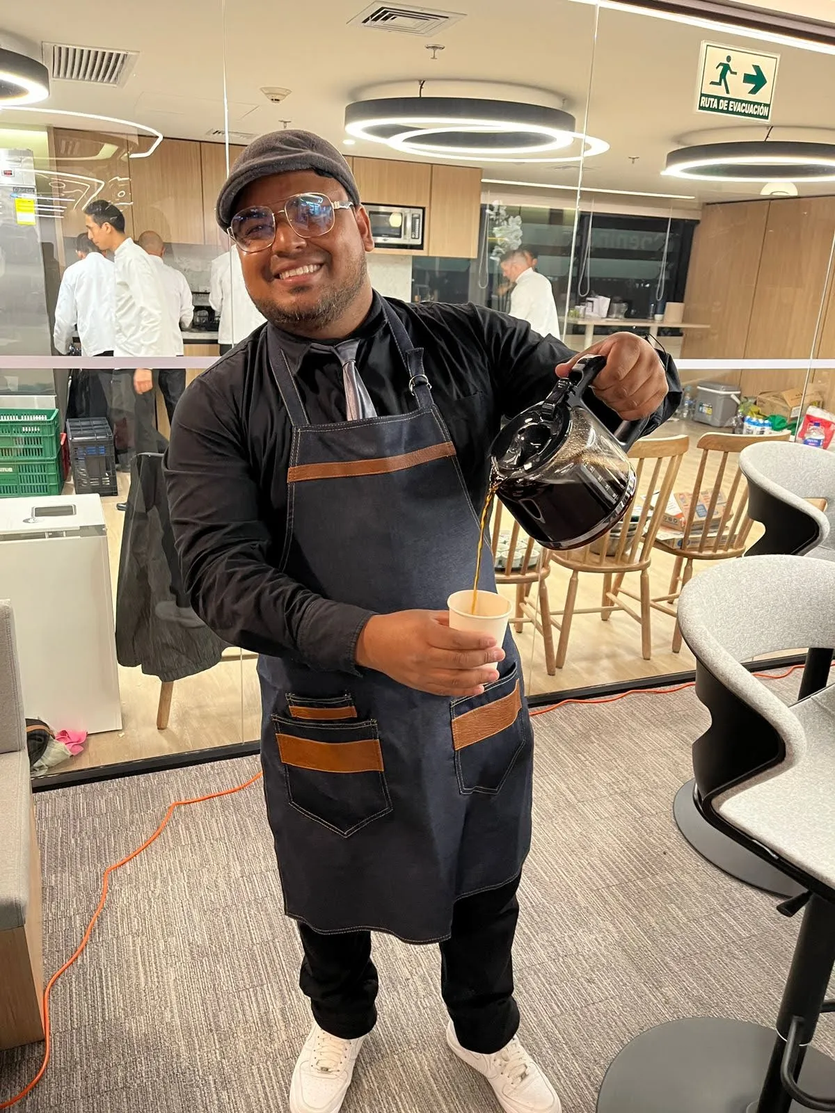 Barista de Experiencia VINTO sirviendo café de una jarra en un vaso de papel durante un evento en una oficina