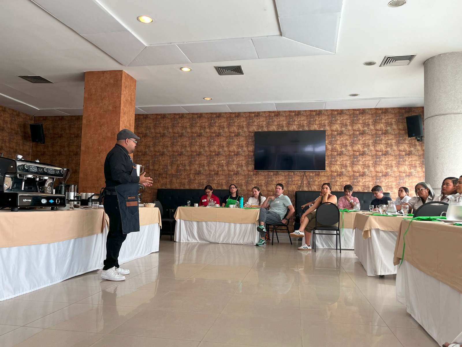 Instructor de Experiencia VINTO guiando una cata de café frente a un grupo sentado en mesas de un salón de eventos