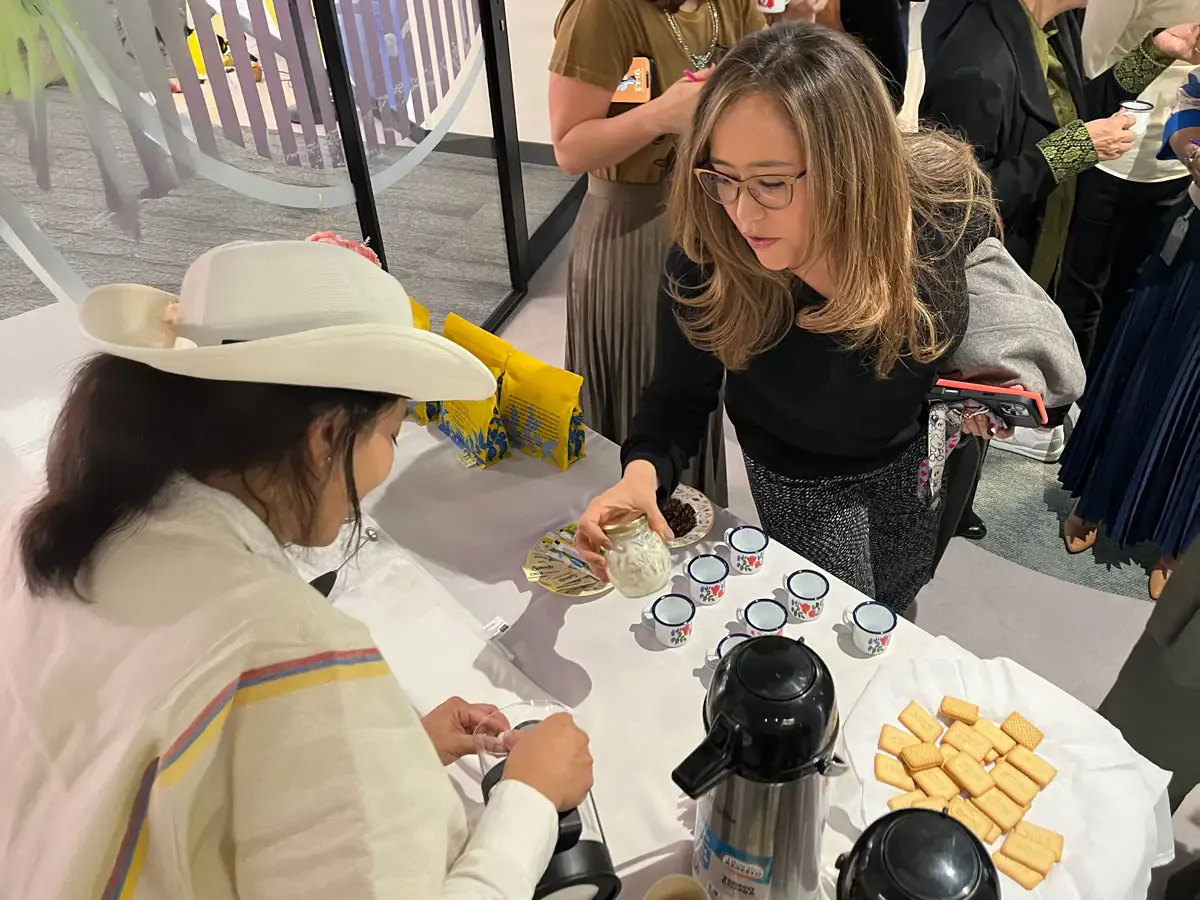 Barista con sombrero y ruana atendiendo a una invitada en una estación de café con termos y pocillos de peltre