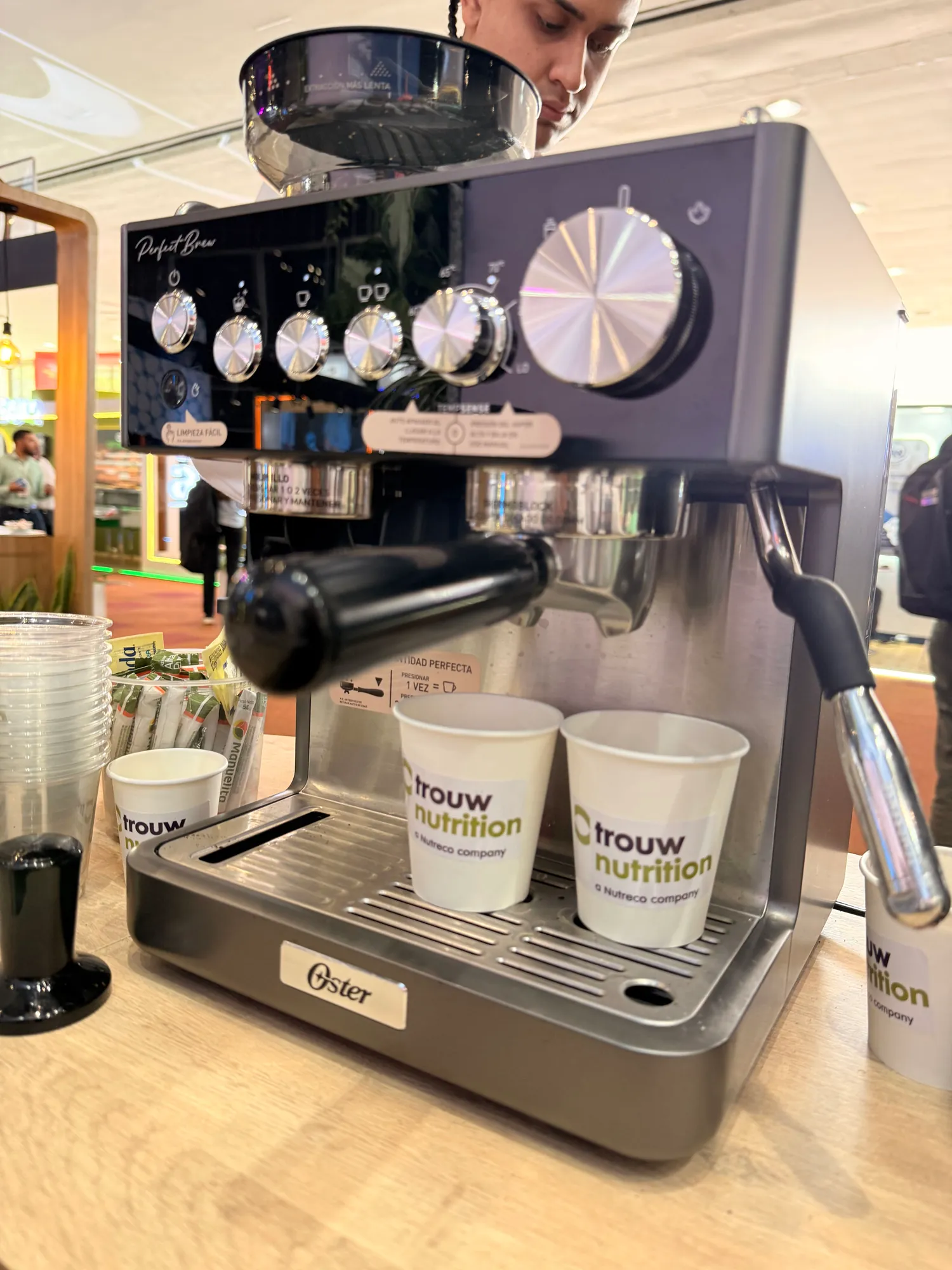 Vasos con la marca Trouw Nutrition en la máquina de espresso de la estación de café del stand