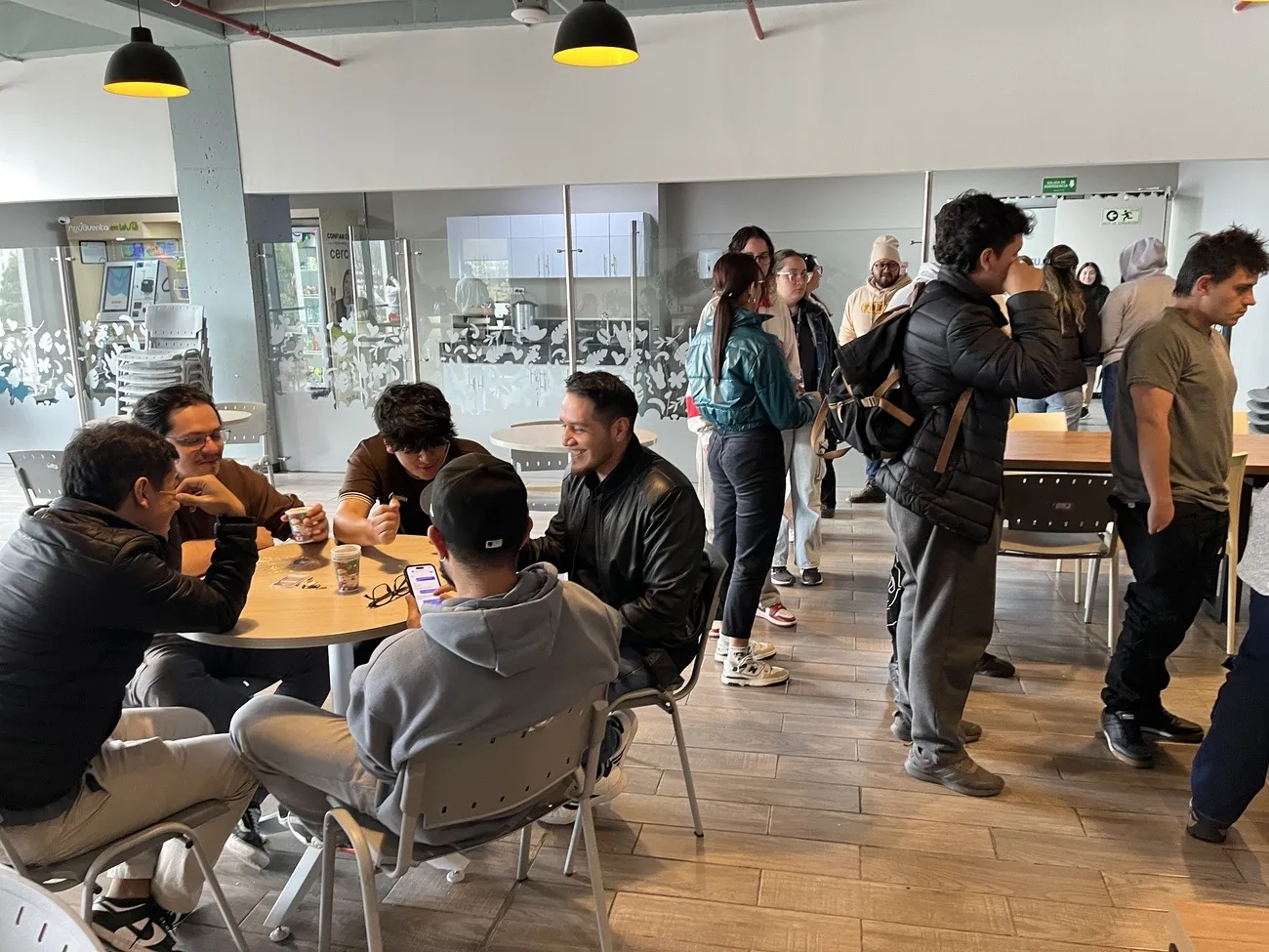 Empleados conversando alrededor de mesas con vasos de café en la cafetería de una oficina